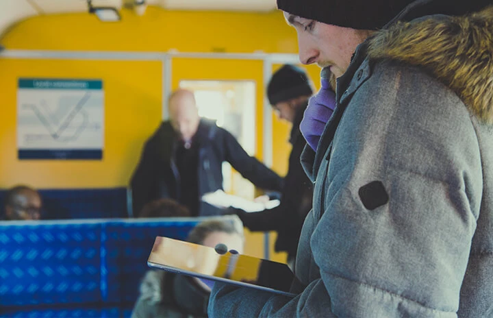 A man in a thick coat on a train looking at an ipad