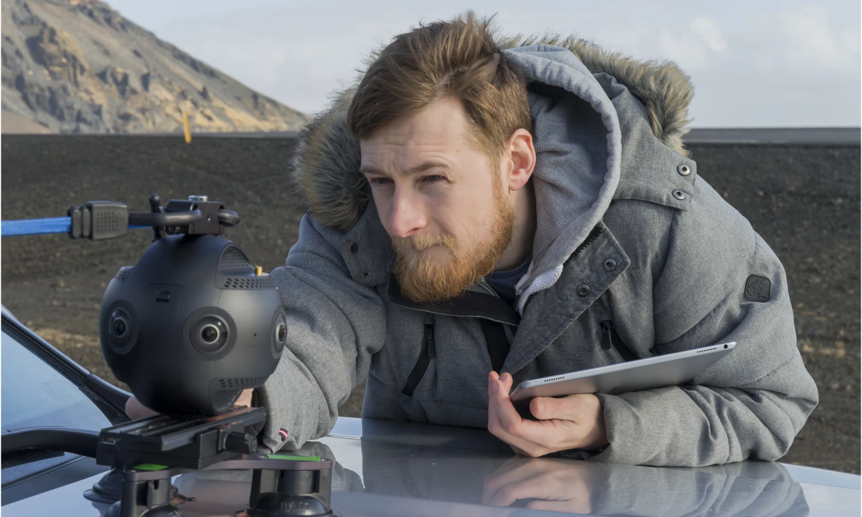 A man in a thick coat adjusting a 360 degree camera attached to the bonnet of a car