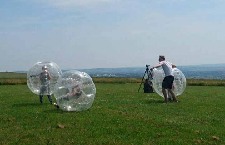 people playing in inflatable orbs being filmed