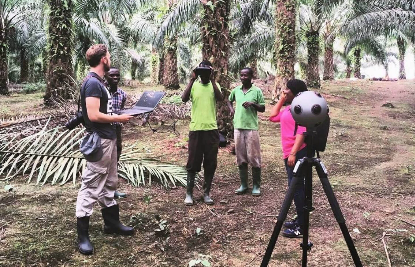 A man filming in a jungle with a 360 degree camera whilst locals take turns viewing footage in a VR headset