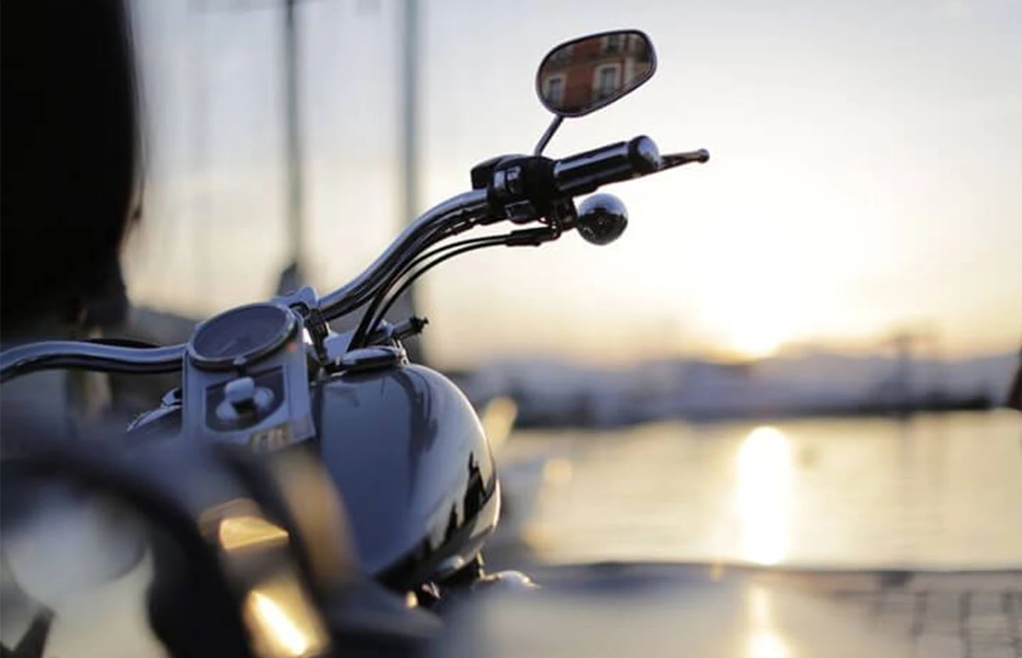 Front of a Harley Davidson motorbike facing a waterside location at sunset