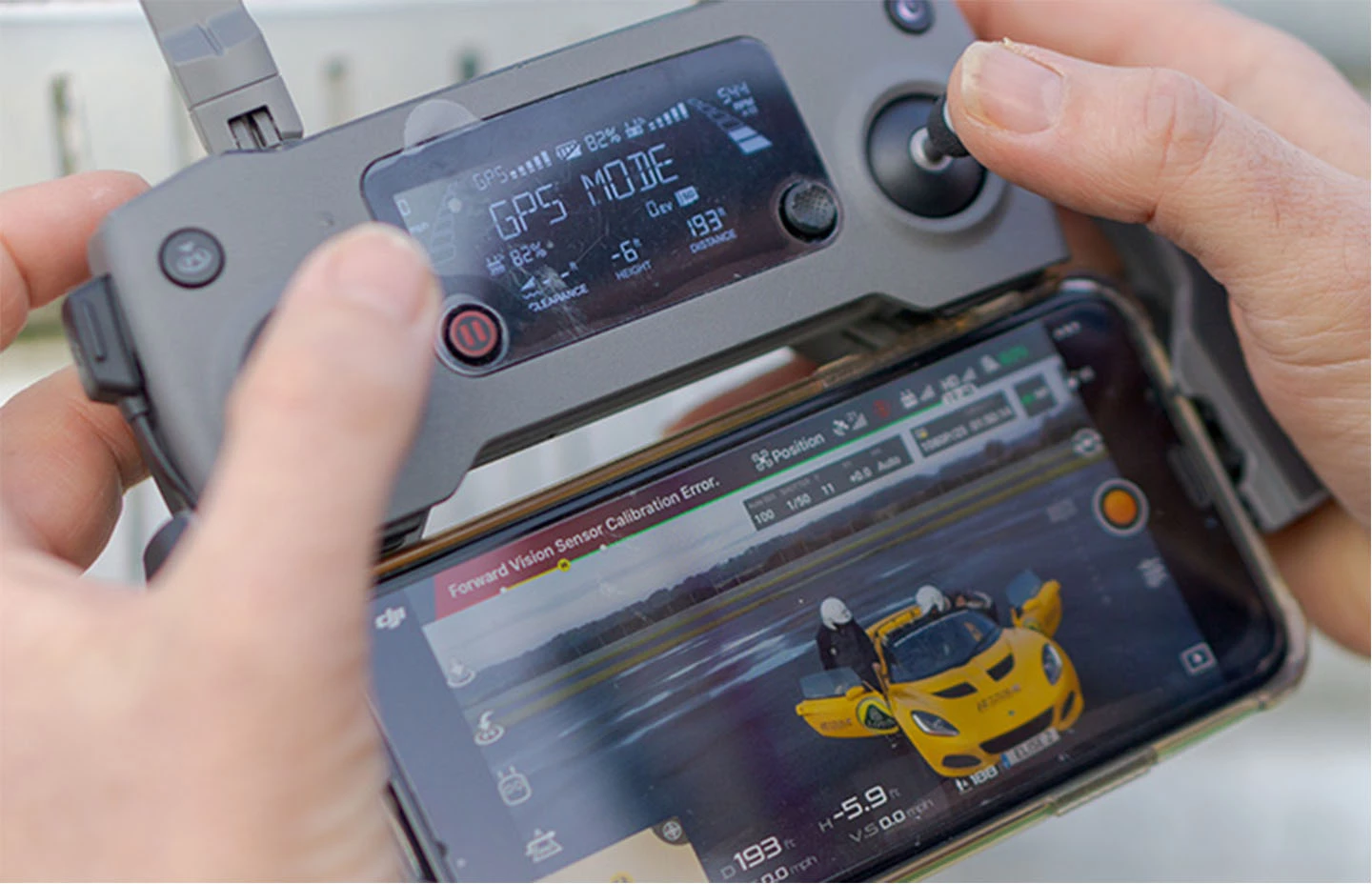 Two hands holding a drone controller with footage of drivers getting in a Lotus on-screen below