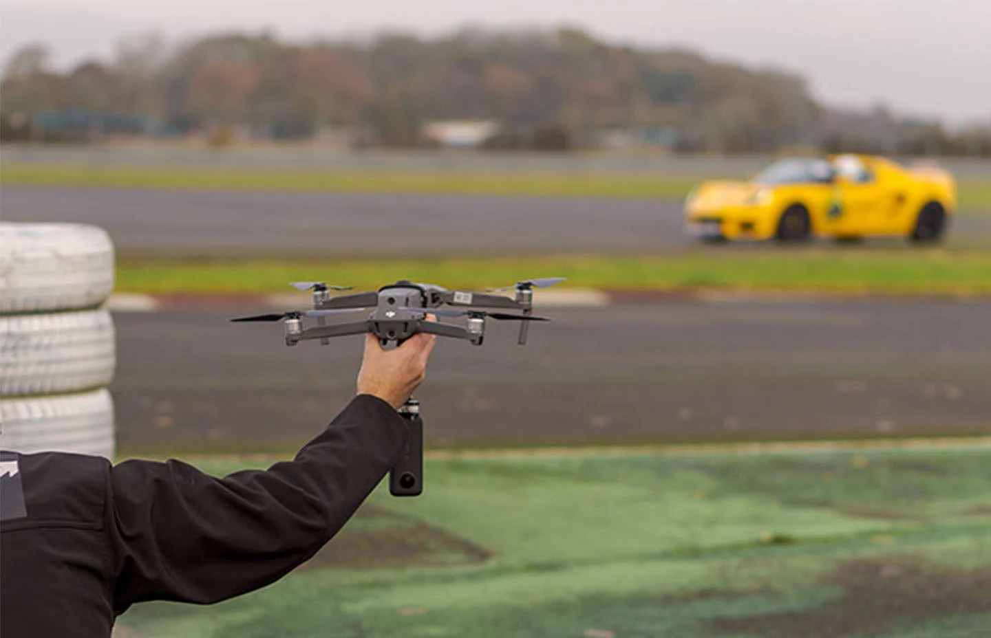 Man holding drone with 360 camera beside a racetrack - yellow Lotus car in the background