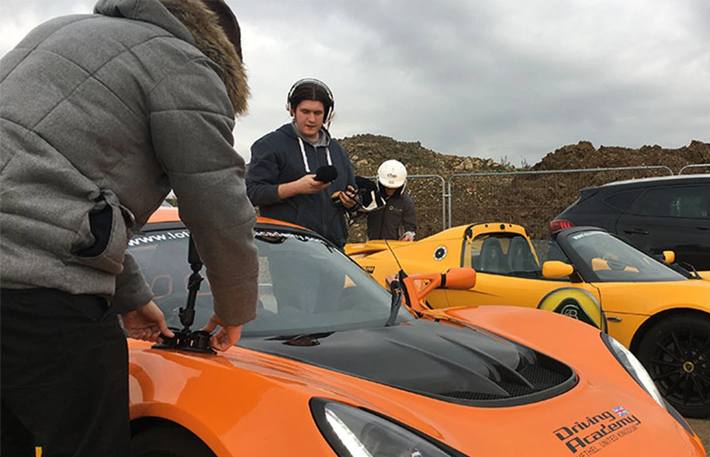 Man setting up a 360 camera on an orange Lotus car with man in headphones and two cars behind him