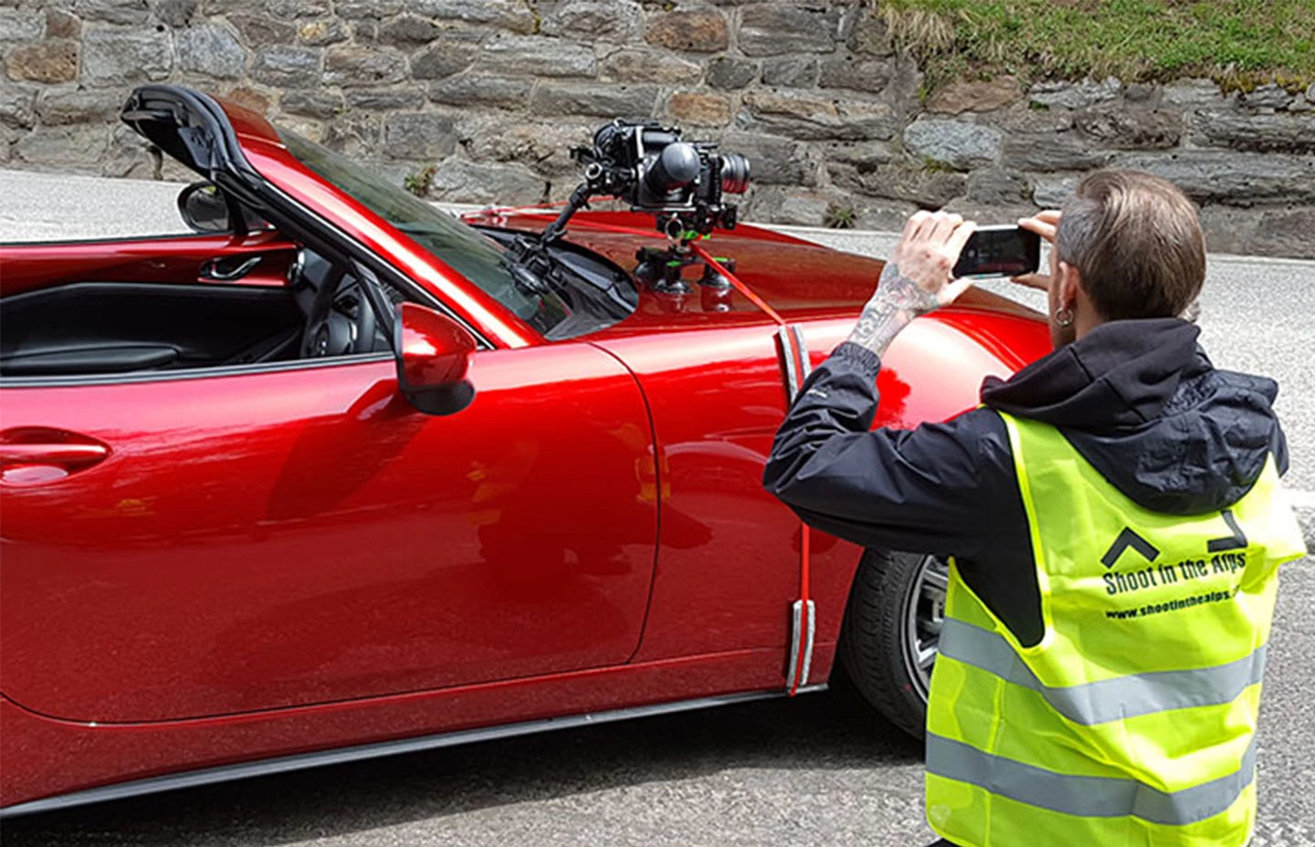 Man kneeling to take a photo of a red Mazda X5 with a 360 camera mounted on the front