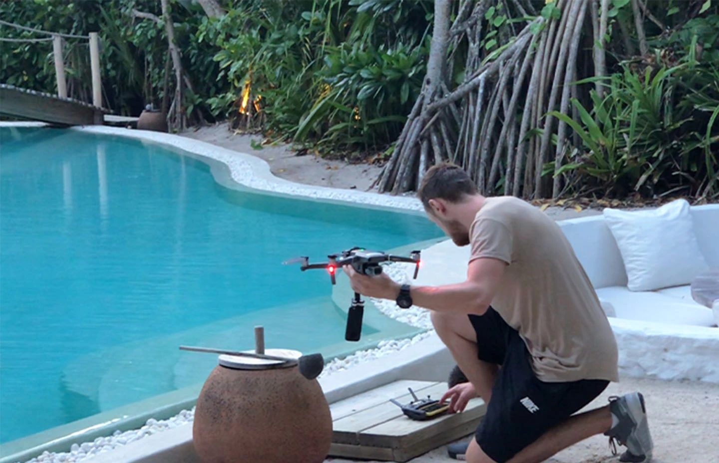 a man holding a drone on his knees in front of a resort pool