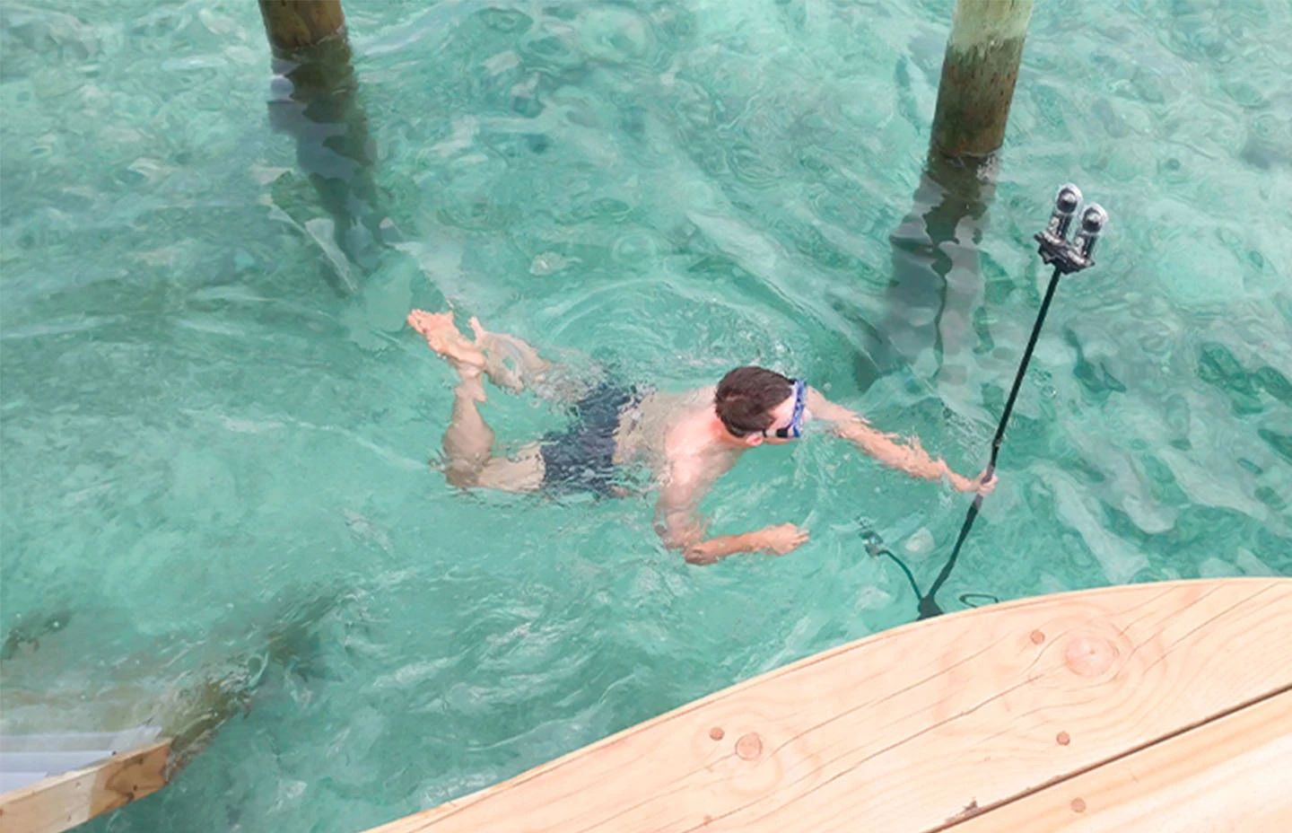 a man swimming whilst holding a 360 degree camera on a pole