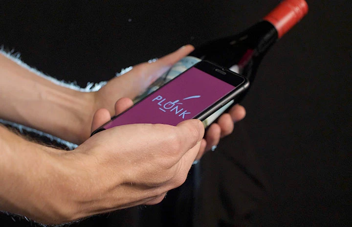 hands holding a bottle of wine and a mobile phone