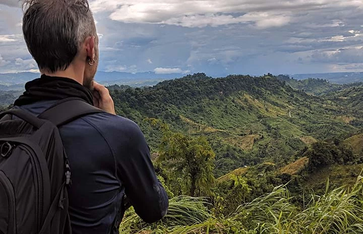 a man dressed in black looking over a lush green mountain range